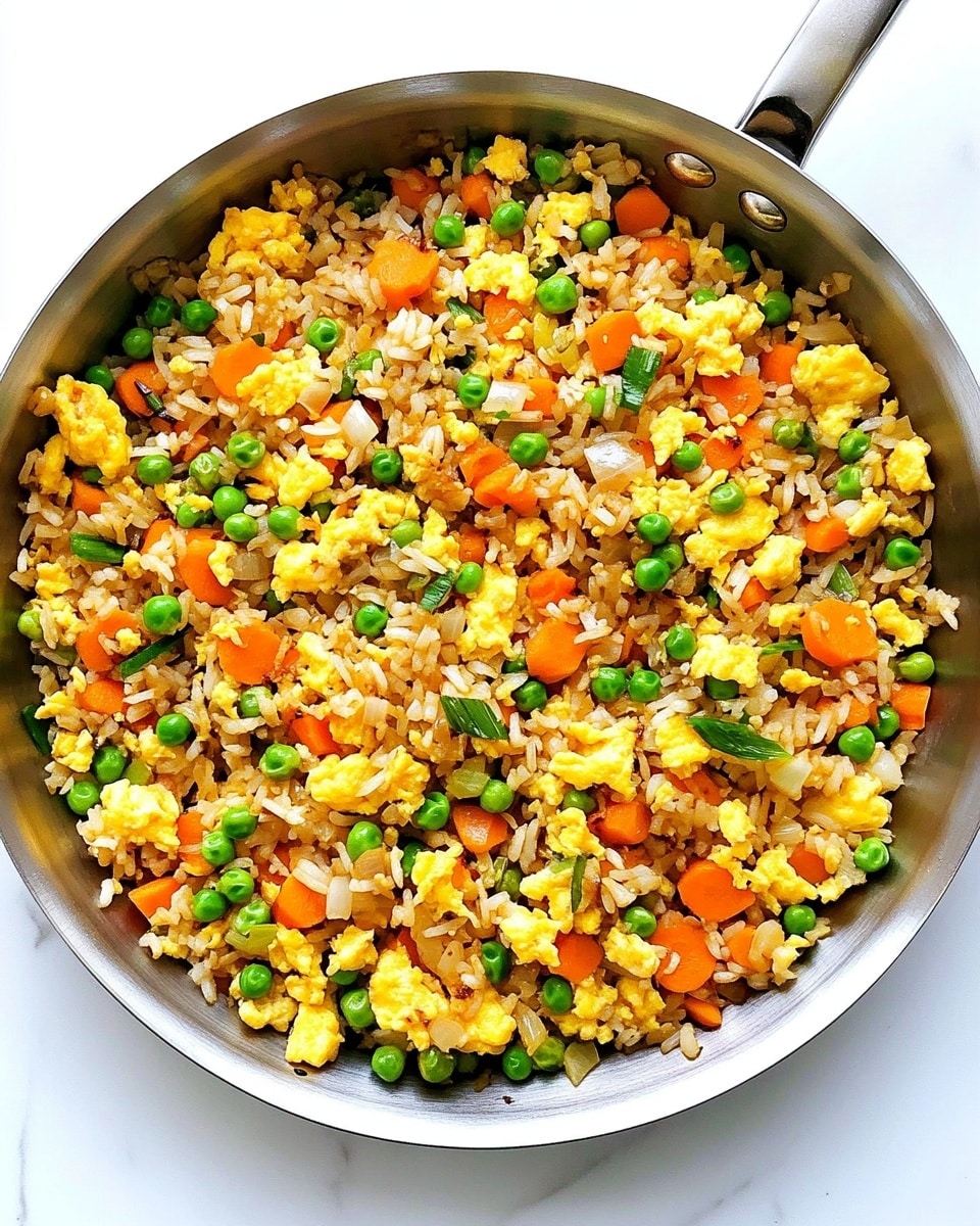 Easy Egg Fried Rice, quick egg fried rice, simple fried rice recipe, homemade egg fried rice, best egg fried rice A close-up of a white bowl full of fried rice, showing a mix of light brown rice grains, bright yellow scrambled eggs, small green peas, chopped red bell peppers, and pieces of cooked onions. The bowl is held by a woman's hand using wooden chopsticks on the left side, picking up some rice. The background and surface are white with a marble texture, making the colors of the food pop. The dish looks fresh and colorful with a mix of soft and slightly crispy textures in the rice and vegetables.