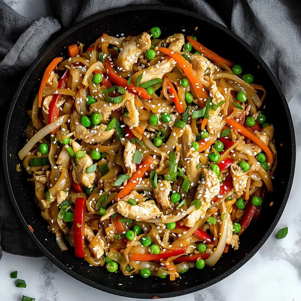 Chicken and Cabbage Stir Fry, easy chicken stir fry, healthy cabbage stir fry, quick weeknight dinner recipes, flavorful stir fry dishes This image shows a black pan filled with a colorful stir-fry. The dish has several layers: small chunks of light beige cooked chicken are mixed with thin strips of red bell pepper, orange carrot, and white onion. Bright green peas and chopped green onions are scattered throughout, adding fresh color. White sesame seeds are sprinkled on top, giving a bit of texture and contrast. The pan rests on a white marbled surface with a dark grey cloth nearby.