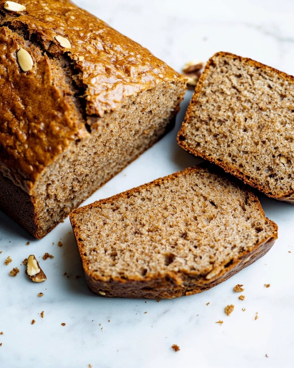 A loaf of brown bread with a shiny, golden-brown crust is shown partially sliced. The bread has a slightly cracked top crust and a soft, dense inside with small bits of nuts or seeds visible. Two slices are placed next to the loaf on a white marbled surface, showing the texture inside. Small crumbs are scattered around the bread, adding a natural touch. Photo taken with an iphone --ar 4:5 --v 6.1