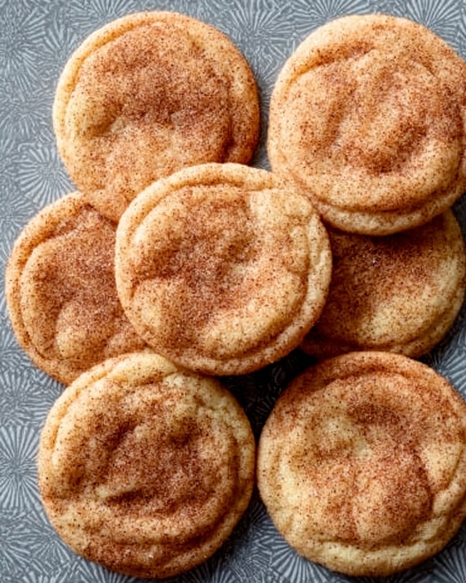 Seven round cookies are placed closely together on a gray patterned surface. Each cookie has a light golden brown color with a dusting of cinnamon sugar on top, giving them a slightly grainy texture. The cookies appear soft with gentle crinkles spread across their tops, showing a slightly raised middle and flatter edges. The overall look is warm and inviting, with the cinnamon sugar adding a sparkling effect. photo taken with an iphone --ar 4:5 --v 7